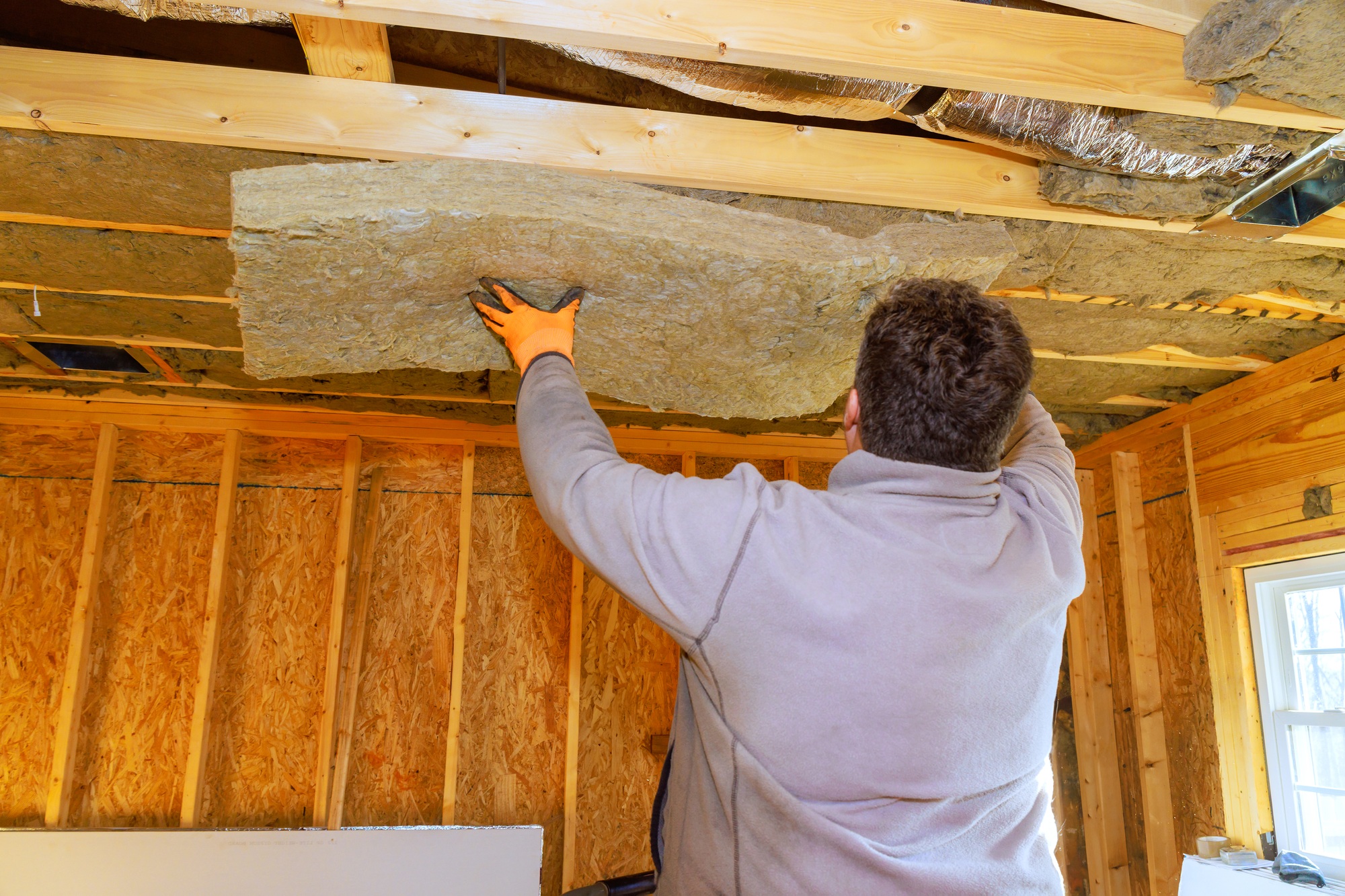 Man installs insulation panels on ceiling during home renovation project in a single-family house